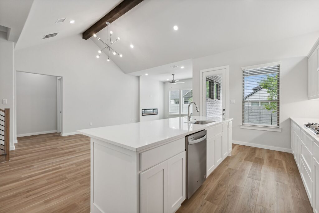 Modern kitchen with white cabinets, a large island, stainless steel appliances, and wood flooring in an open layout—perfect for entertaining. Enjoy bright living areas and spacious design in homes for sale in McKinney Texas.
