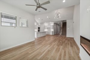 Open-concept living area with wood flooring, modern ceiling fans, white walls, visible kitchen, and staircase leading upstairs—perfect for those seeking Painted Tree McKinney homes for sale.
