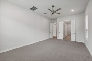 Empty, carpeted room with a ceiling fan, white walls, and two open doors leading to a hallway and bathroom. Natural light enters through a window on the right—one of many inviting spaces in homes for sale in McKinney, Texas.