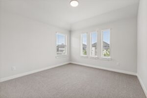 Empty room with light gray carpet, white walls, and four tall windows with blinds letting in natural light, offering a bright view—perfect for those seeking Painted Tree homes for sale in McKinney, Texas.