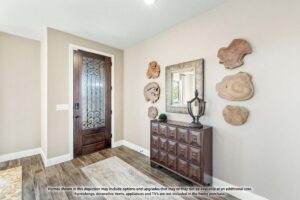 Entryway with a wooden door, wall-mounted wood art, a mirror, and a dark dresser on a light-colored wall—showcasing the charm found in Painted Tree homes for sale. Text with a home purchase disclaimer at the bottom.