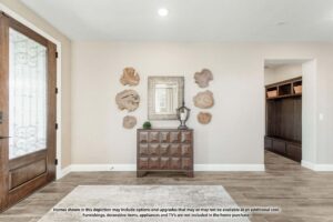 Bright entryway with a wooden front door, wood cabinet with a lamp, mirror, natural wood wall art, and tiled floors. A hallway with built-in storage is visible to the right in this charming Painted Tree McKinney home.