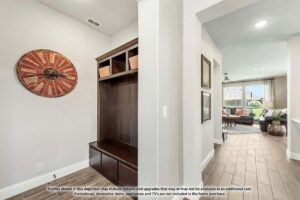 Entryway with a built-in dark wood bench and storage, large red wall clock, and view into a living room with neutral decor and large windows—perfect inspiration for those seeking homes for sale in McKinney, Texas.