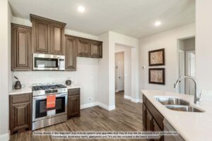 Modern kitchen with dark wood cabinets, stainless steel appliances, built-in microwave, gas stove, white countertops, and double sink on light wood flooring—perfect for those seeking homes for sale in McKinney Texas.