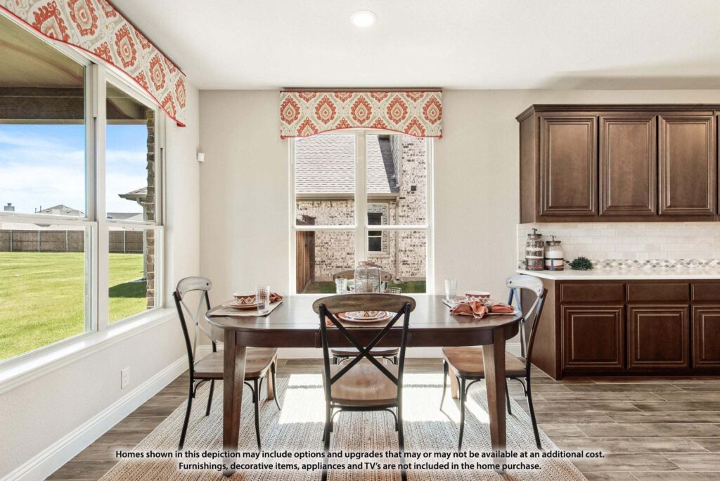A dining area with a rectangular table set for four, large windows with red-patterned valances, and dark wood cabinets highlights the bright, modern style of Painted Tree homes for sale in McKinney, Texas.