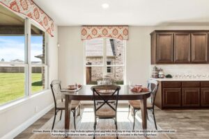 A dining area with a rectangular table set for four, large windows with red-patterned valances, and dark wood cabinets highlights the bright, modern style of Painted Tree homes for sale in McKinney, Texas.