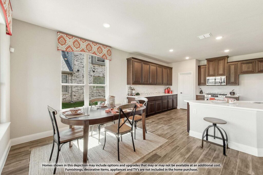 Bright kitchen and dining area with wooden cabinets, a round table set for four, barstools at a counter, large windows, and neutral tones—all in one of the desirable Painted Tree McKinney homes for sale.