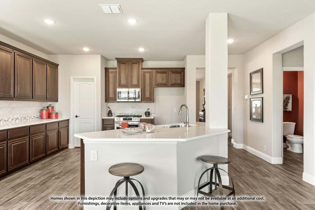 Modern kitchen with dark wood cabinets, stainless steel appliances, a white island with two stools, and tile flooring; a hallway and bathroom are visible in the background—ideal for those seeking Painted Tree homes for sale.