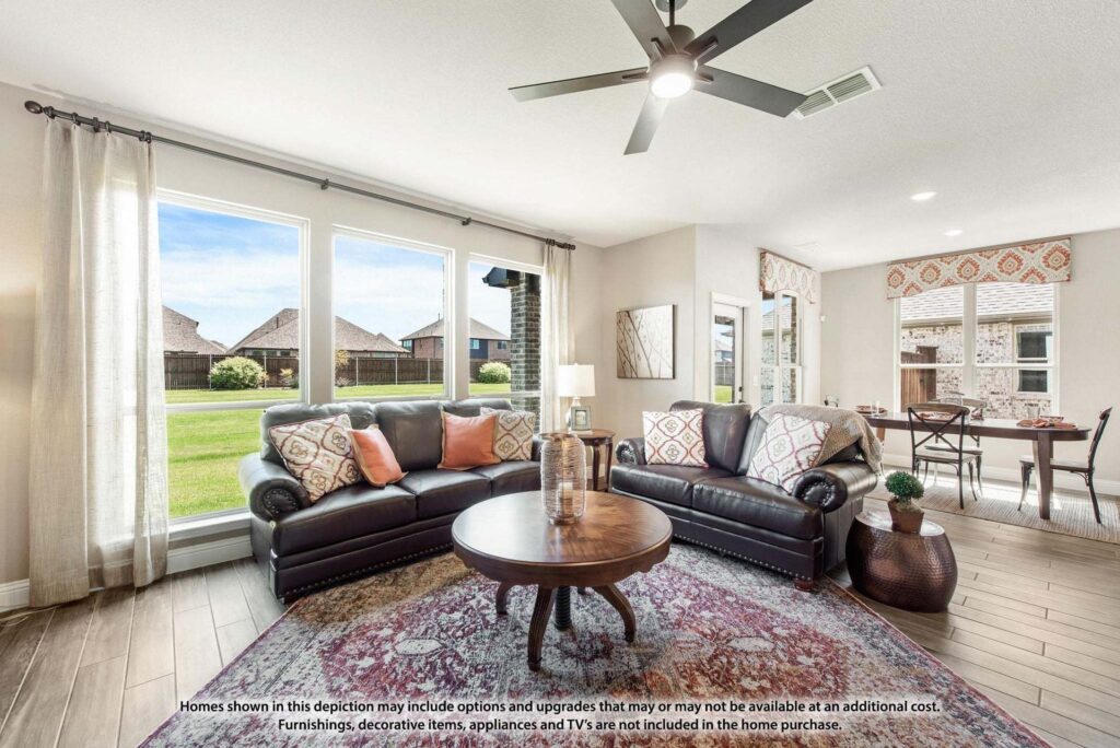 A bright living room with two dark leather sofas, a round coffee table, and large windows overlooking a green lawn; dining area visible in the background—perfect for those seeking painted tree homes for sale in McKinney, Texas.