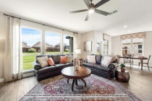 A bright living room with two dark leather sofas, a round coffee table, and large windows overlooking a green lawn; dining area visible in the background—perfect for those seeking painted tree homes for sale in McKinney, Texas.