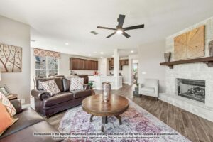 Modern open-concept living room with dark leather sofas, round wooden coffee table, fireplace, and view into a kitchen with white cabinets and stainless steel appliances—perfect for those seeking Painted Tree homes for sale in McKinney, Texas.