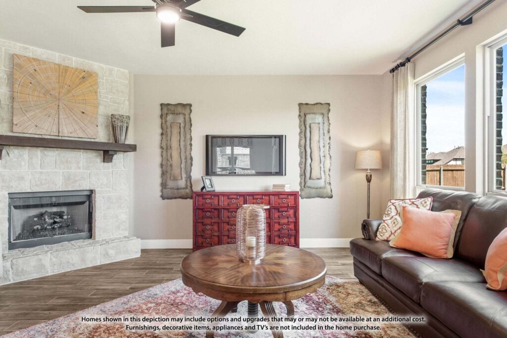 Modern living room with a stone fireplace, ceiling fan, TV on the wall above a red cabinet, round wooden coffee table, and brown leather sofa with pillows—perfect for those seeking homes for sale in McKinney Texas.