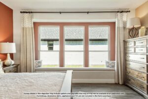 Bedroom with three large windows, beige curtains, a wooden dresser, a lamp, and window seating with decorative pillows; informational text is visible along the bottom edge—discover homes for sale in McKinney Texas like this.
