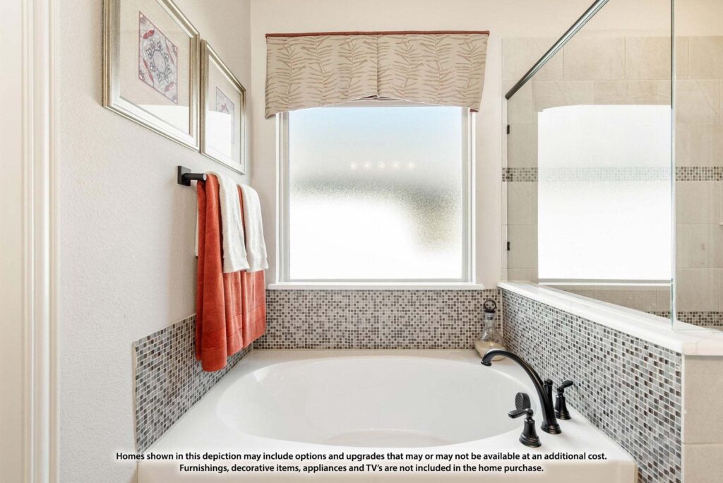 Modern bathroom with a white bathtub, mosaic tile accents, black fixtures, red and white towels, frosted window, and wall art—perfect for relaxing in homes for sale in McKinney Texas.