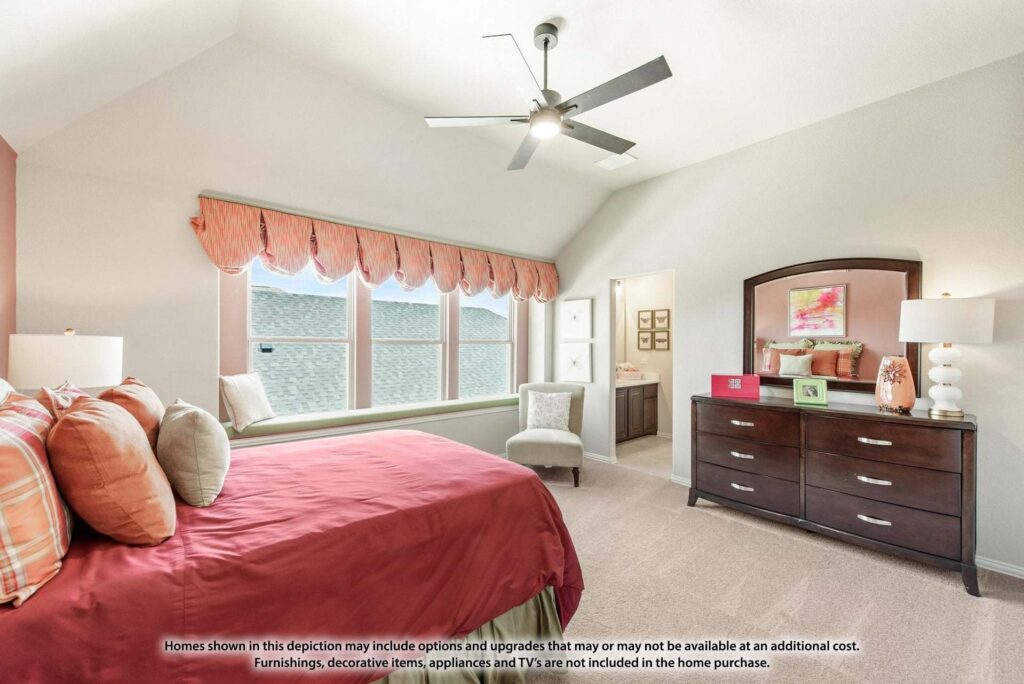 A bedroom with a red bedspread, pillows, dresser with mirror, bedside lamps, and large windows with valances—just one inviting space you’ll find in Painted Tree McKinney homes for sale. A doorway leads to an adjoining bathroom.