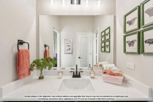 Modern bathroom in Painted Tree McKinney with a white countertop, black faucet, orange towels, potted plant, and framed butterfly prints. Decorative items not included in homes for sale in McKinney Texas.
