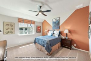 A neatly arranged bedroom in Painted Tree TX features a blue bed, orange accent wall, ceiling fan, nightstand, and framed wall art. A large window fills the space with natural light—perfect for those seeking homes for sale in McKinney Texas.