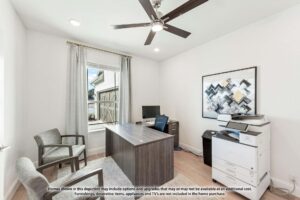 Modern home office with a wooden desk, two chairs, a printer, and abstract wall art. A ceiling fan with lights is overhead, and sunlight streams through the large curtained window—ideal for those searching homes for sale in McKinney Texas.