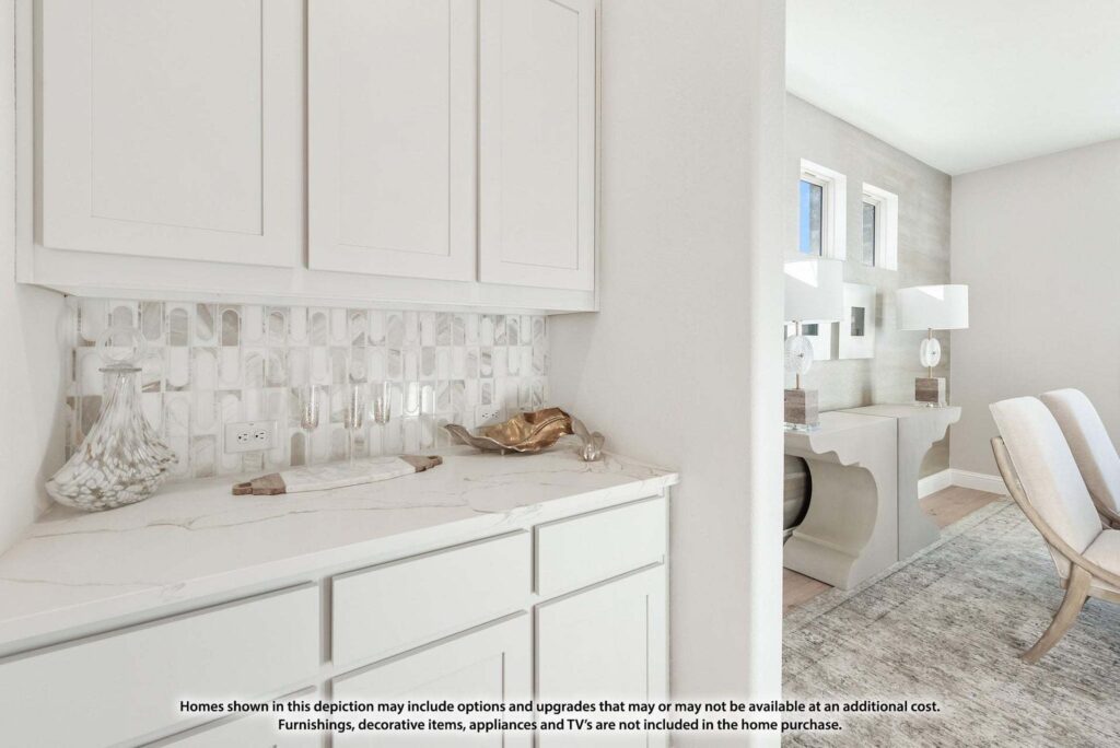 White cabinetry with marble countertop and backsplash, decorative items on the counter, and a view into a bright, modern room with a desk and chair—perfect for those seeking Painted Tree homes for sale in McKinney, Texas.