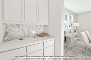 White cabinetry with marble countertop and backsplash, decorative items on the counter, and a view into a bright, modern room with a desk and chair—perfect for those seeking Painted Tree homes for sale in McKinney, Texas.