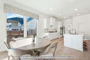 A modern kitchen and dining area with white cabinets, a round wooden table, kitchen island, and large windows letting in natural light—perfect for those seeking Painted Tree McKinney homes for sale.