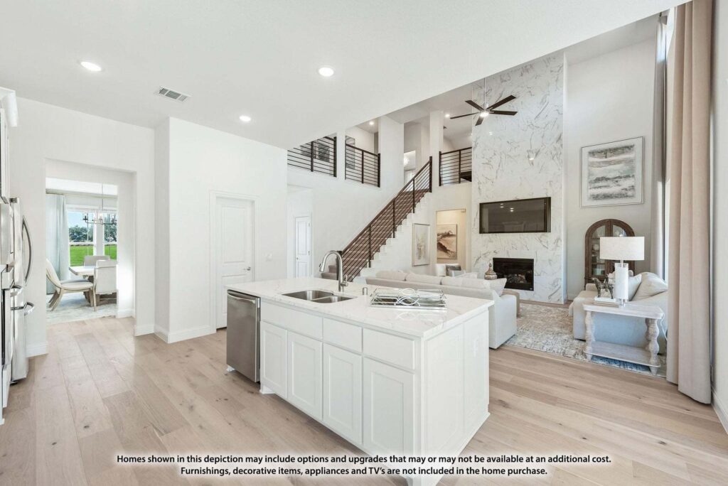 Modern open-concept living area in Painted Tree McKinney, featuring a white kitchen island, stainless sink, and adjacent living room with high ceilings, large windows, and a stylish staircase with railing.