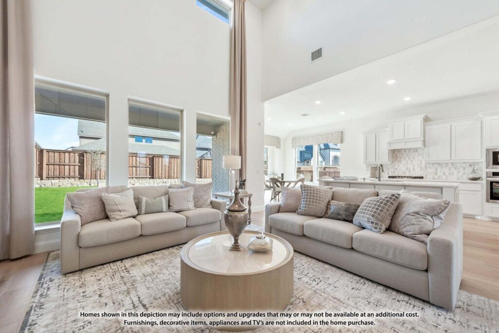A modern living room with two light-colored sofas, a round coffee table, large windows, and an open kitchen in the background—perfect for those exploring Painted Tree homes for sale in charming McKinney, Texas.