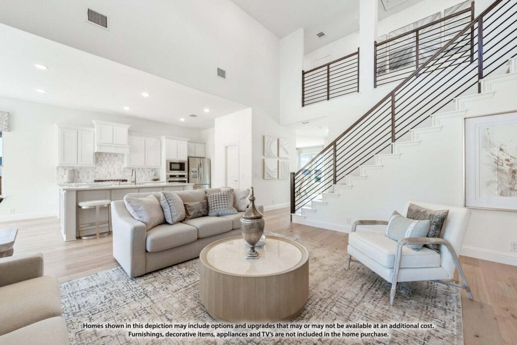Modern living room with neutral-toned furniture, a round coffee table, open kitchen in the background, and a staircase with metal railings—perfect for those seeking homes for sale in McKinney, Texas, near Painted Tree.