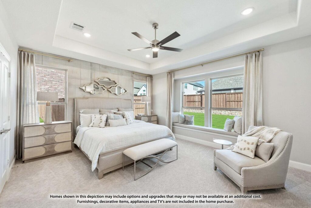 Bright, modern bedroom with a large bed, bench, armchair, dresser, and neutral decor. Large windows offer views of a fenced backyard—perfect for those seeking stylish comfort in homes for sale in McKinney Texas.