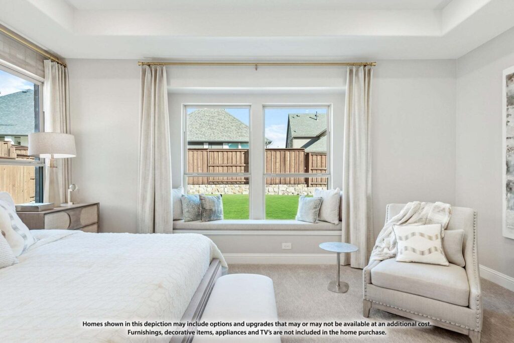 Bright bedroom with a large window seat, neutral decor, and an upholstered chair, overlooking a fenced backyard with neighboring houses—perfect for those exploring homes for sale in McKinney Texas.