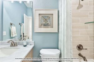 Modern bathroom with sink, toilet, wall art, towel, and beige tiled shower; text at the bottom notes items may not be included in home purchase. Discover more like this among Painted Tree homes for sale in McKinney, Texas.