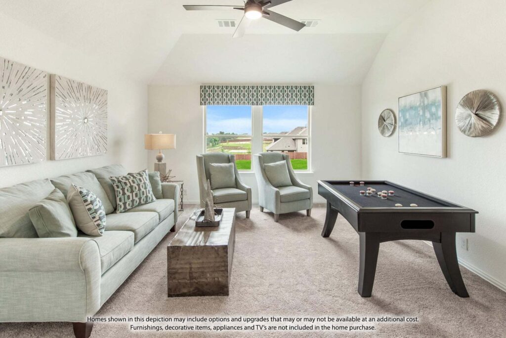 Modern living room with light-colored sofas, wooden coffee table, wall art, and pool table under a ceiling fan. Large window shows a suburban neighborhood view in the heart of Painted Tree McKinney.