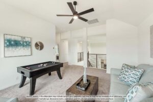 A modern loft space with a sofa, coffee table, wall art, and a small pool table, featuring neutral decor and a ceiling fan—perfect for those seeking Painted Tree McKinney living or homes for sale in McKinney, Texas.