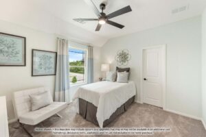 A neatly decorated bedroom in Painted Tree McKinney features a single bed, a white chair, wall art, a window with curtains, a ceiling fan, and neutral-colored walls—perfect for those exploring homes for sale in McKinney, Texas.
