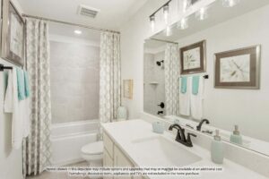 Modern bathroom with a white vanity, black fixtures, and a bathtub with gray tile surround—just one of the elegant features you'll find in homes for sale in McKinney, Texas. Teal and white towels add a fresh touch to this beautiful space.