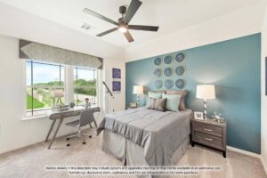 Modern bedroom with a blue accent wall, bed, nightstands, and a desk by large windows. Decorative clocks and pillows add style; enjoy an outdoor view reminiscent of Painted Tree McKinney homes for sale.