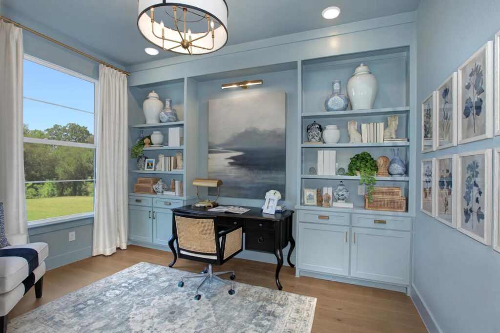 Home office with blue built-in shelves, a black desk, decorative vases, books, and art on the wall. A large window fills the space with light—perfect for remote work in one of the stylish homes at Painted Tree McKinney.