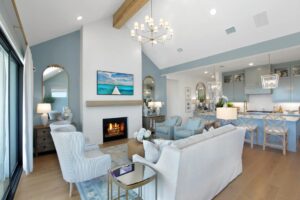A modern open-concept living room and kitchen in blue and white decor, featuring a lit fireplace, large windows, and wooden ceiling beams—perfect for those seeking Painted Tree TX homes for sale in McKinney, Texas.