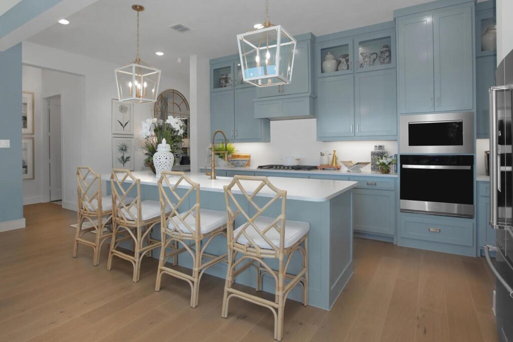 Modern kitchen with light blue cabinets, white countertops, island seating with four bamboo chairs, stainless steel appliances, and pendant lighting—a perfect fit for Painted Tree TX or anyone seeking stylish homes for sale in McKinney Texas.