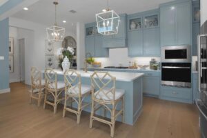 Modern kitchen with light blue cabinets, white countertops, island seating with four bamboo chairs, stainless steel appliances, and pendant lighting—a perfect fit for Painted Tree TX or anyone seeking stylish homes for sale in McKinney Texas.