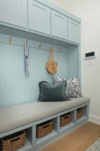 A built-in light blue mudroom bench with cushion, throw pillows, wall hooks holding a bag and leash, and four wicker baskets in cubbies below—perfect for homes for sale in McKinney Texas like those in Painted Tree McKinney.