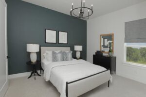 Modern bedroom with a white bed, dark accent wall, two lamps on side tables, a black dresser with a mirror, and a window with a gray shade—perfect for those seeking Painted Tree McKinney homes for sale.