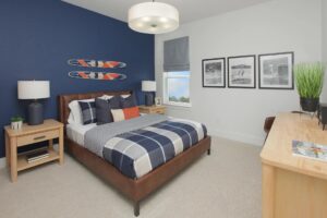 A modern bedroom with a blue accent wall, bed with plaid bedding, two bedside tables, wall-mounted skis, three framed photos, a window, and a wooden desk with a plant—styled just like homes found in Painted Tree McKinney.