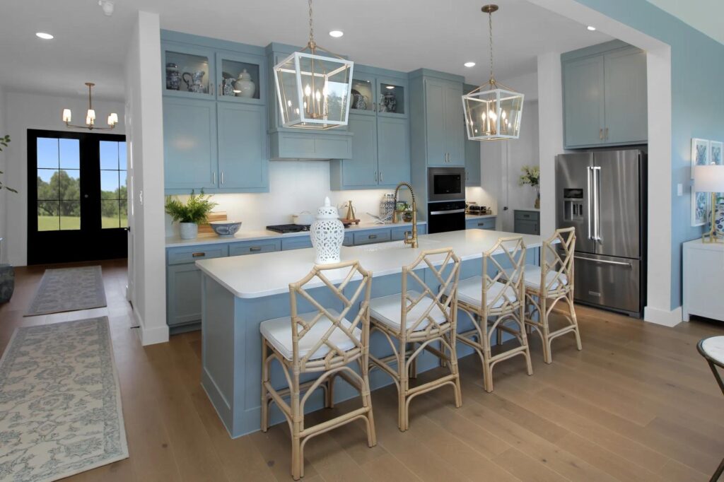 Modern kitchen with blue cabinets, a large island with four wooden chairs, stainless steel appliances, pendant lights, and decorative items—perfect for those seeking Painted Tree McKinney or homes for sale in McKinney Texas.