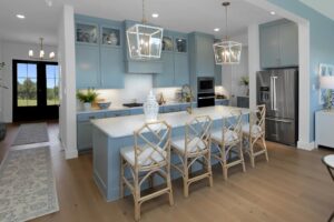 Modern kitchen with blue cabinets, a large island with four wooden chairs, stainless steel appliances, pendant lights, and decorative items—perfect for those seeking Painted Tree McKinney or homes for sale in McKinney Texas.