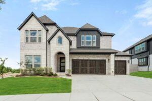 Two-story modern house with light brick exterior, dark trim, and three-car garage on a manicured lawn under a partly cloudy sky—discover stunning Painted Tree McKinney homes for sale in this sought-after community.