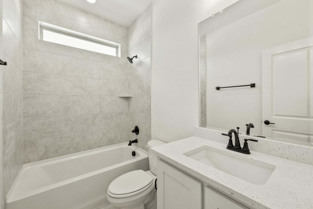 Modern bathroom in Painted Tree McKinney with a bathtub-shower combo, white vanity and sink, large mirror, and black fixtures. Light-colored tile and walls create a bright, clean look perfect for homes for sale in McKinney Texas.