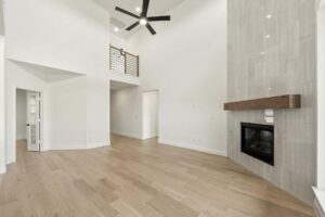 Spacious modern living room in one of the stunning Painted Tree TX homes for sale, featuring light wood floors, high ceilings, a wood mantel fireplace, ceiling fan, and a loft area with railing.