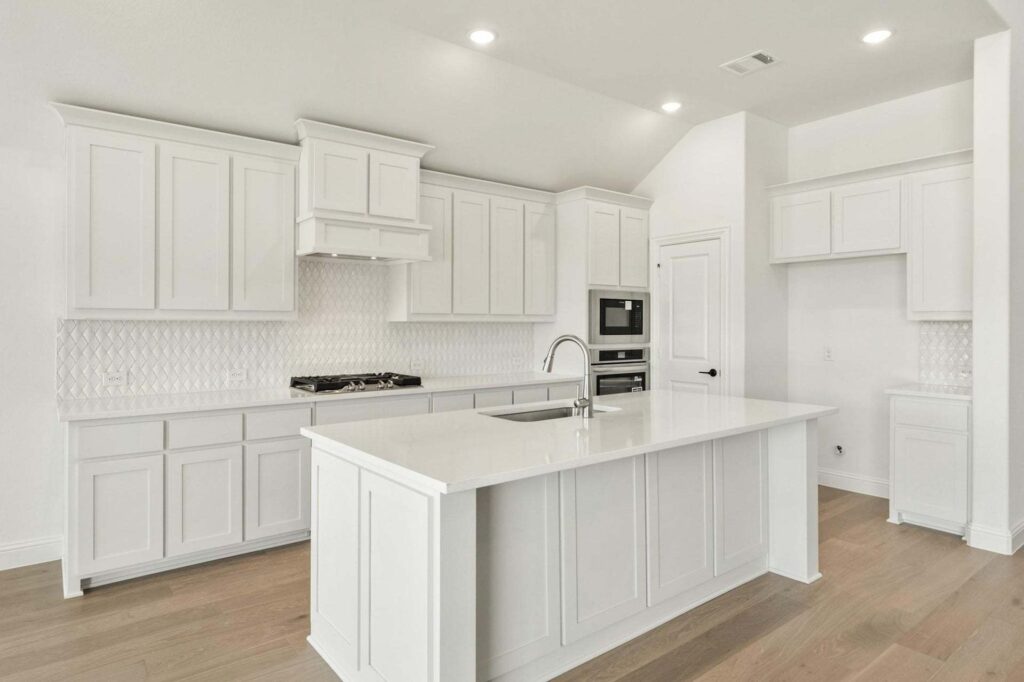 Modern kitchen in Painted Tree McKinney featuring white cabinets, white countertops, built-in oven, gas stove, tile backsplash, and a central island with sink. Enjoy light wood flooring and recessed lighting throughout.
