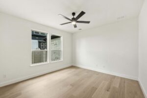 Empty room with light wood flooring, white walls, two windows, ceiling vent, and a sleek black modern ceiling fan—perfect for those seeking Painted Tree McKinney homes for sale or elegant living in Painted Tree TX.